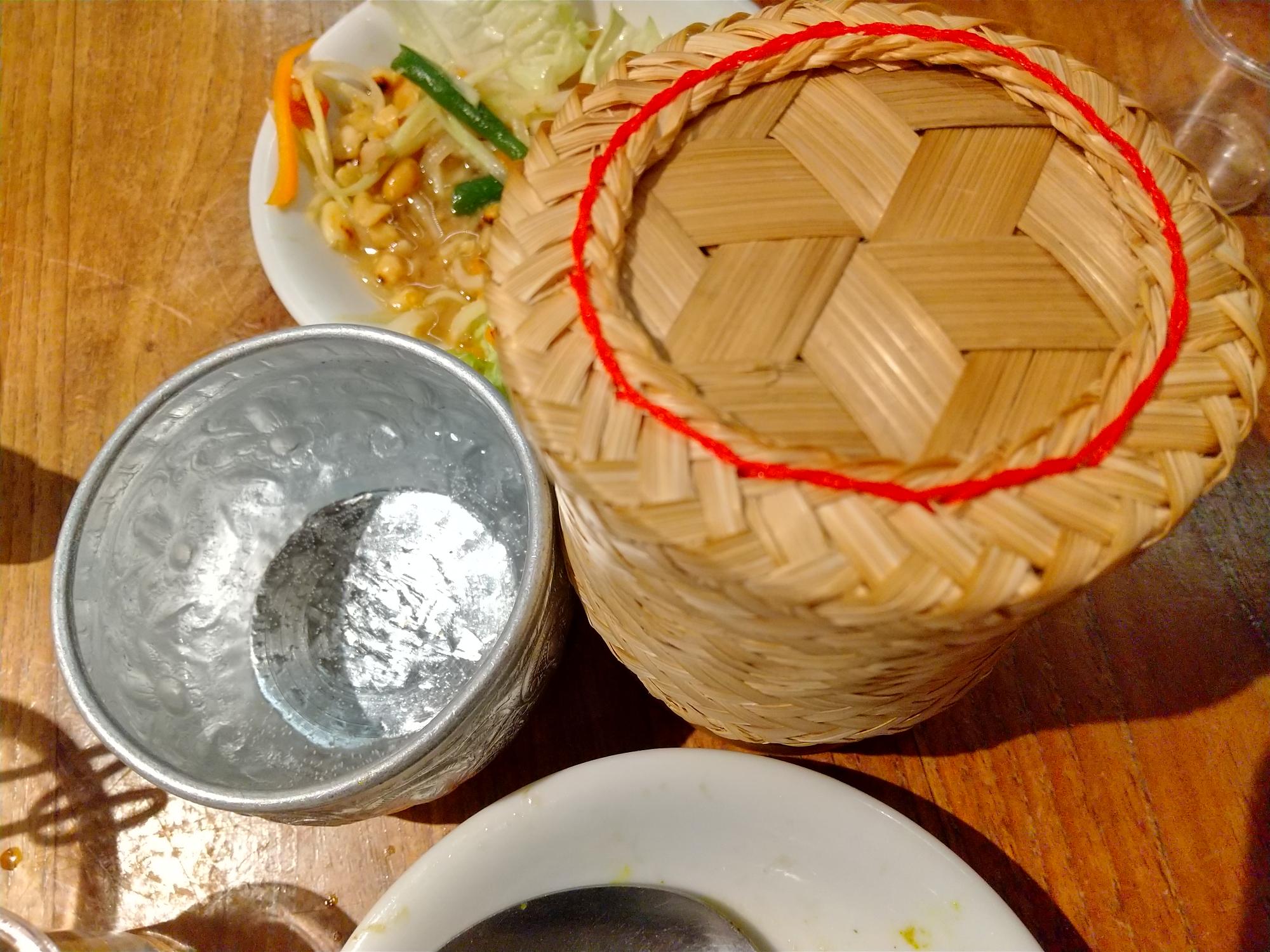 ソースが残ったら、竹細工に入ったカオニャオ（餅米）をからめていただく。タイ東北部は米どころなのだ。左がタイで多くとれるスズのコップ。夏はこれで水を飲むと冷え冷え～