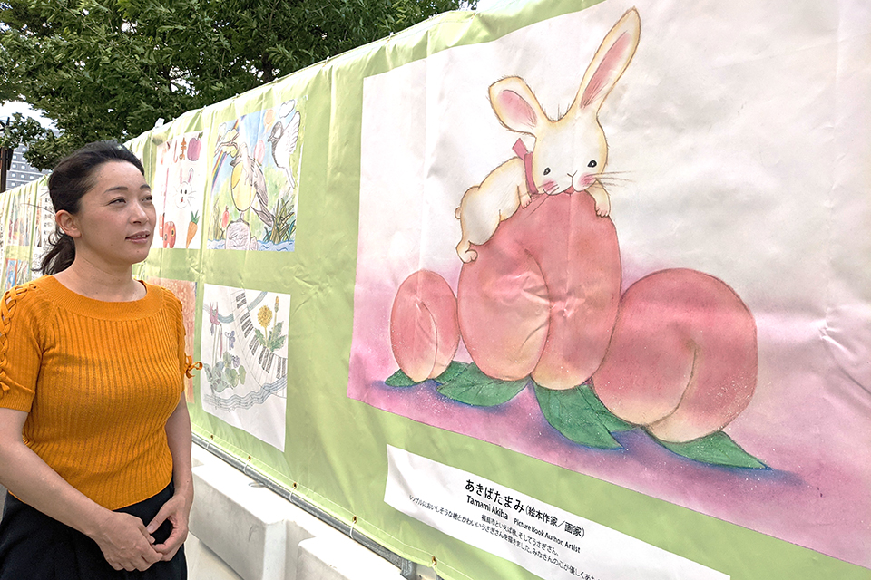 福島市在住の絵本作家で画家のあきばたまみさん。福島の特産品である桃と、吾妻山の種まきウサギをイメージした作品とともに。